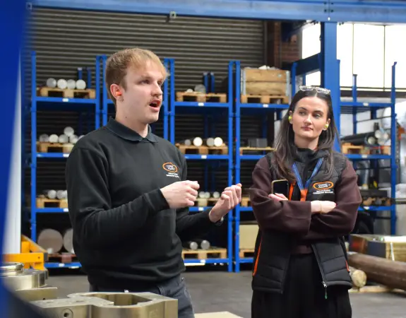 Two colleagues discussing work in an industrial warehouse setting.